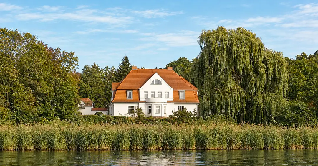 Der Gutshof Schwielowsee vom Wasser aus gesehen, mit Schilfgürtel im Vordergrund